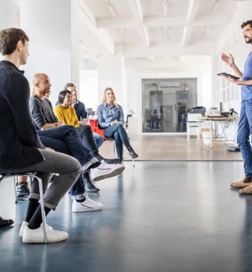 Young man discussing new ideas with team at a meeting. Businessman speaking in front of small audience at office meeting.